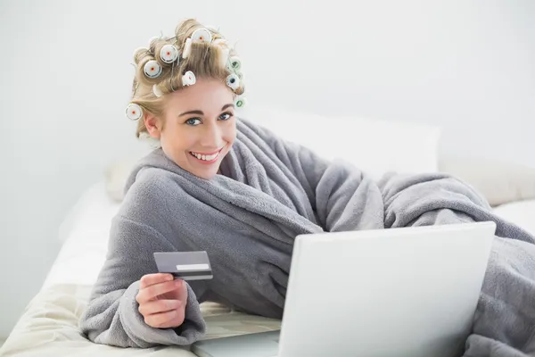 Joyful relaxed blonde woman in hair curlers buying online with her laptop — Stock Photo, Image