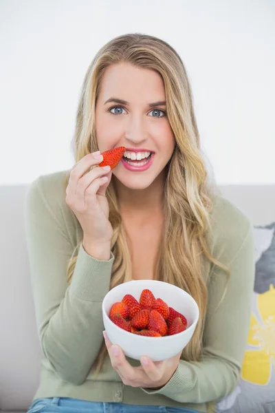 Gelukkig schattige blonde eten aardbeien zittend op de gezellige sofa — Stockfoto