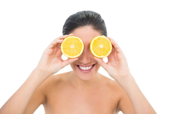 Bonita morena sosteniendo dos mitades naranjas sobre sus ojos — Foto de Stock