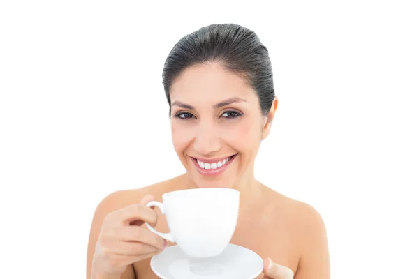 Atractiva morena sosteniendo una taza y platillo y sonriendo a la cámara — Foto de Stock