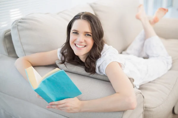 Vrolijke mooie vrouw liggend op een gezellige Bank lezen van boek — Stockfoto