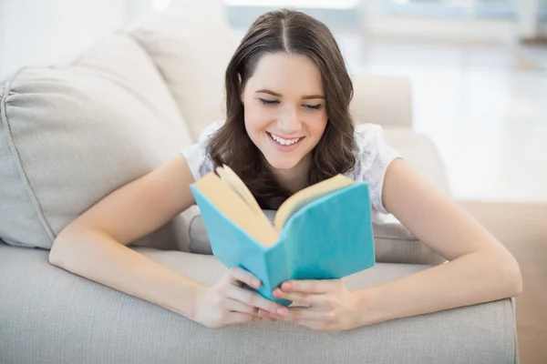 Wanita cantik yang damai berbaring di sofa yang nyaman membaca buku — Stok Foto