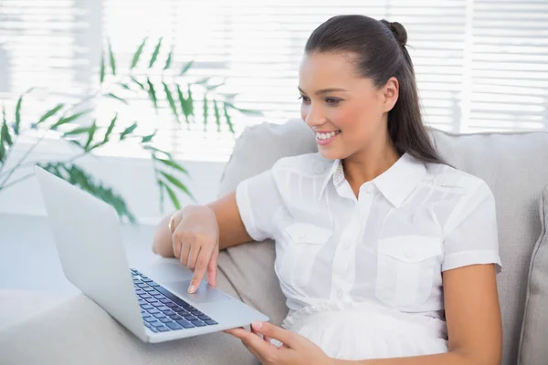 Cheerful pretty woman using laptop sitting on cosy sofa — Stock Photo, Image