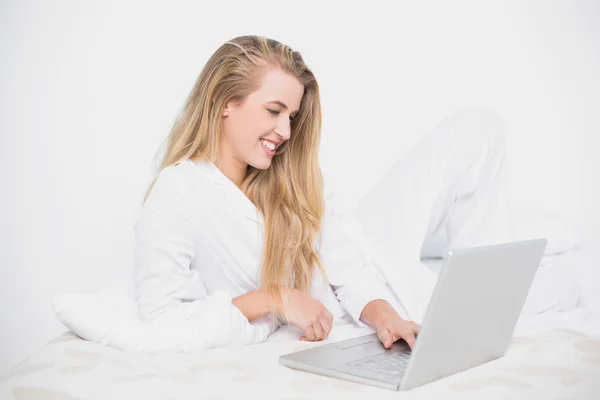 Smiling pretty model using her laptop lying on cosy bed — Stock Photo, Image