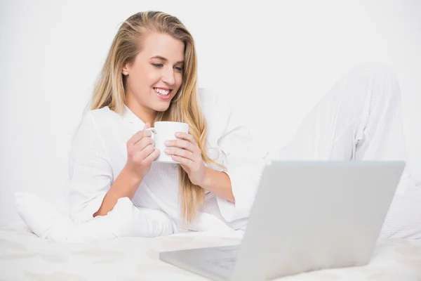 Sonriendo modelo lindo sosteniendo café acostado en la cama acogedora —  Fotos de Stock