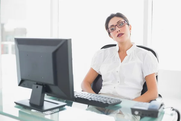 Mulher de negócios franzina sentada em sua mesa olhando para o computador — Fotografia de Stock