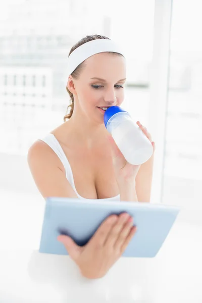 Fridfullt vackra idrottskvinna dricksvatten medan du använder TabletPC — Stockfoto