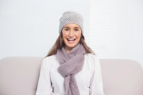 Morena sorridente com chapéu de inverno sentado no sofá acolhedor — Fotografia de Stock