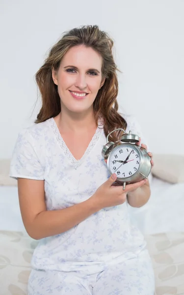 알람 시계를 들고 침대에 앉아 웃는 여자 — 스톡 사진