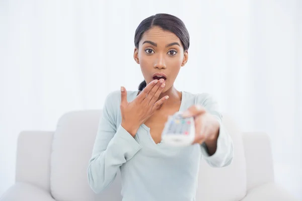 Shocked cute woman sitting on sofa changing tv channel — Stock Photo, Image