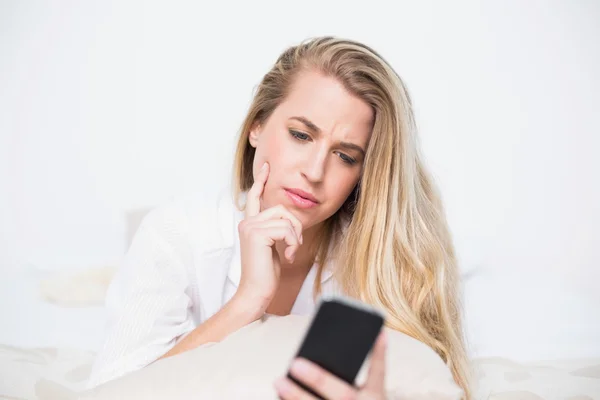 Fronsen model houden haar smartphone liggend op gezellige bed — Stockfoto