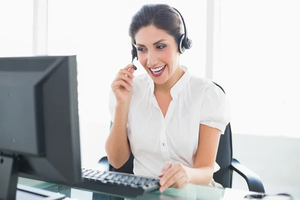 Laughing call centre agent sitting at her desk on a call