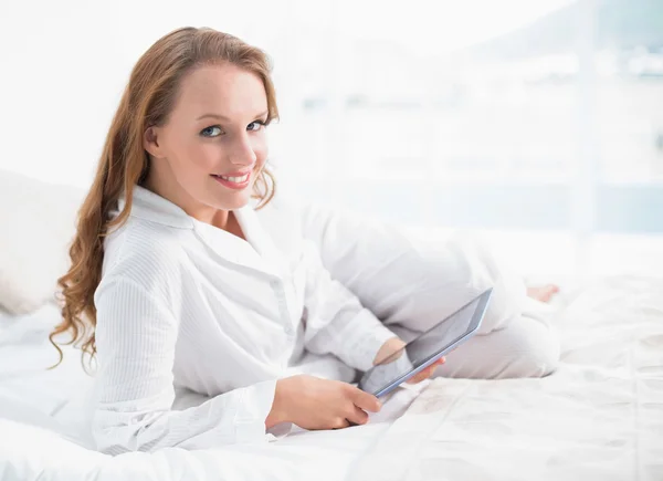 Friedliche hübsche Frau mit einem Tablet-PC auf ihrem Bett liegend — Stockfoto
