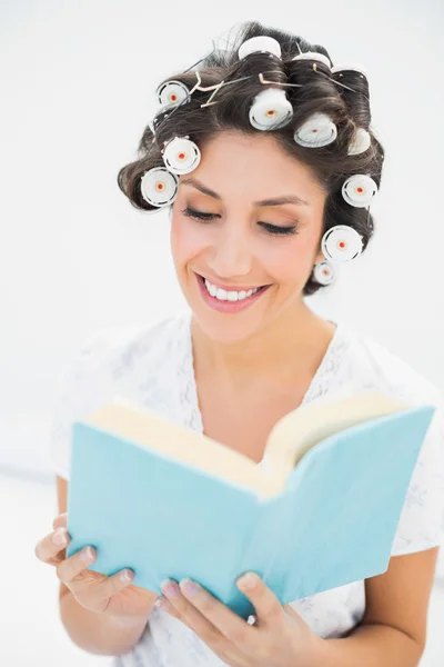 Fröhliche Brünette in Haarrollen liest ein Buch auf dem Bett — Stockfoto