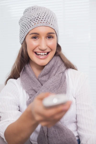 Smiling brunette with winter hat on holding remote — Stock Photo, Image