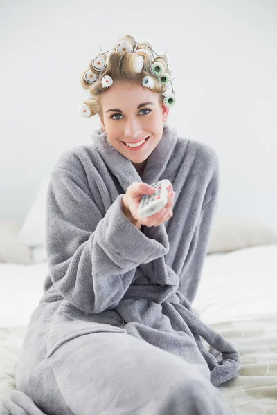 Joyful relaxed blonde woman in hair curlers using a remote control — Stock Photo, Image