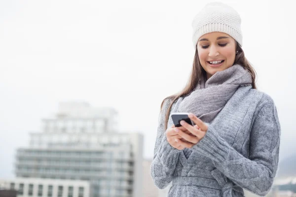 Smiling young woman with winter clothes on text messaging — Stock Photo, Image