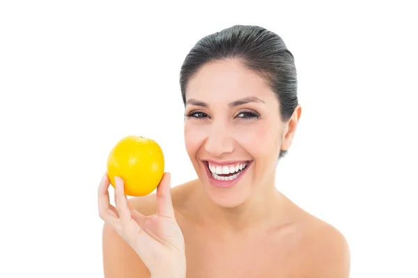 Sonriente morena sosteniendo una naranja y mirando a la cámara — Foto de Stock