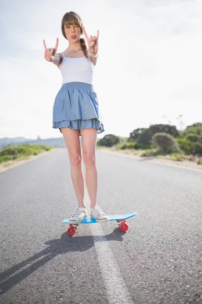 时尚女人制作摇滚手势时她的滑板上的平衡 — 图库照片