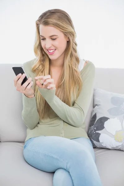 Uśmiechający się ładny blond SMS siedząc na kanapie przytulny — Zdjęcie stockowe
