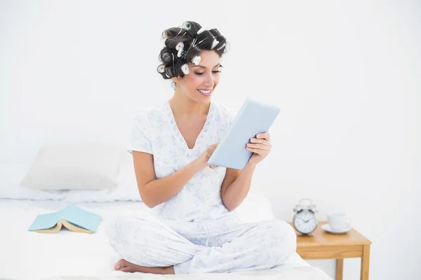 Pretty brunette in hair rollers using tablet on bed — Stock Photo, Image