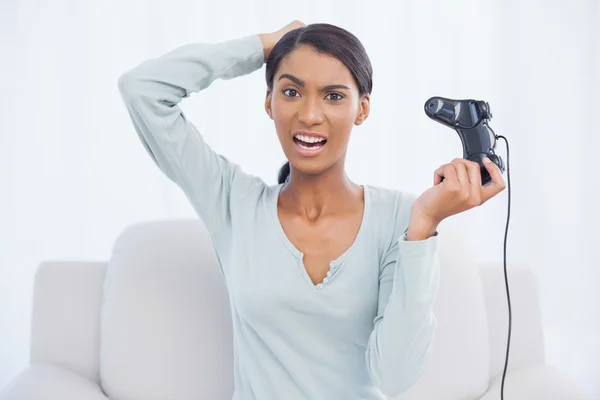 Раздраженная красивая женщина, сидящая на диване и играющая в видеоигры — стоковое фото