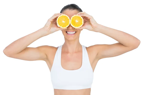 Mujer sonriente en forma sosteniendo rodajas de naranja en sus ojos —  Fotos de Stock