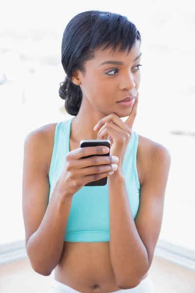 Femme en forme pensive tenant un téléphone portable — Photo