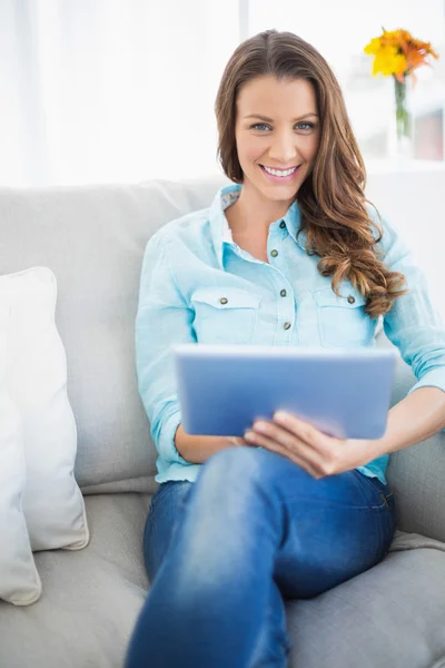 Lockande brunett sitter på soffan med hjälp av Tablet PC — Stockfoto