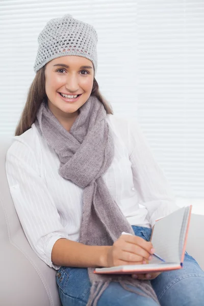 Sorridente bella bruna con cappello invernale sulla scrittura sul suo taccuino — Foto Stock