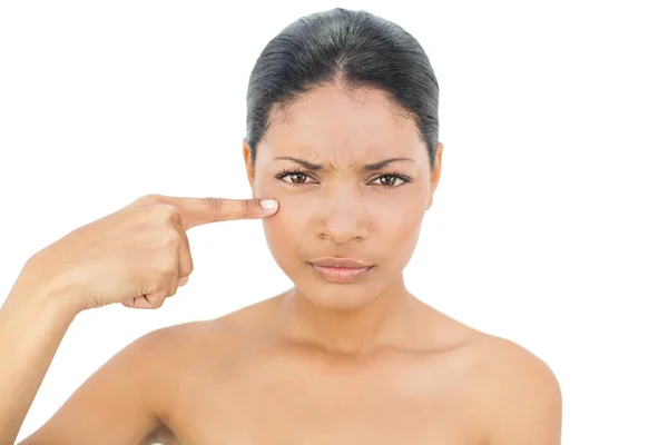 Frowning black haired model pointing at her cheek — Stock Photo, Image