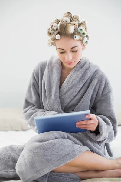 Mujer rubia relajada concentrada en rulos de pelo usando una tableta pc — Foto de Stock