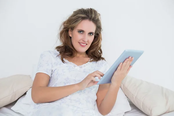 Leende kvinna i sängen med hjälp av Tablet PC — Stockfoto