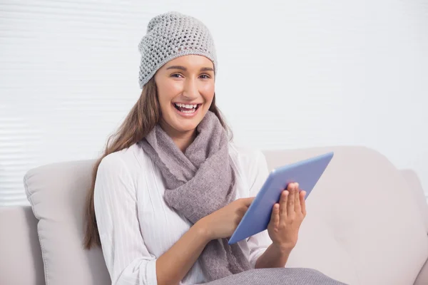 Sorridente bruna carina con cappello invernale su scorrimento sul suo tablet — Foto Stock