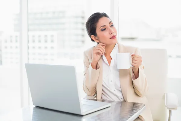 Pensativa mujer de negocios sosteniendo taza mientras trabaja en el ordenador portátil — Foto de Stock