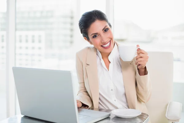 Feliz mujer de negocios sosteniendo taza mientras trabaja en el ordenador portátil — Foto de Stock