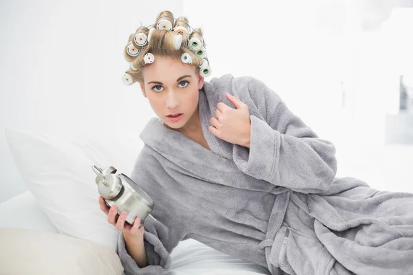 Mujer rubia preocupada en rulos de pelo sosteniendo un despertador —  Fotos de Stock