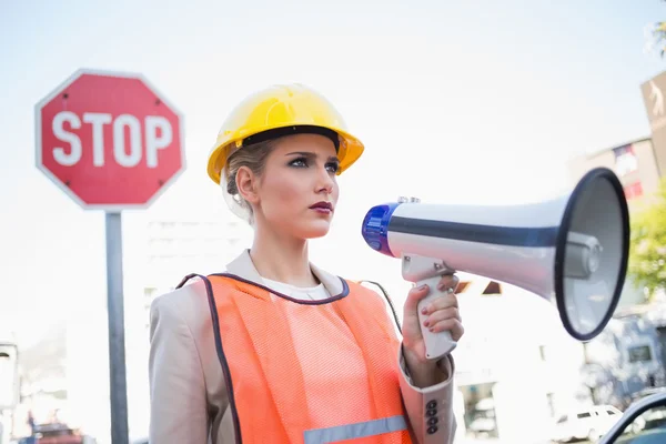 Frowning businesswoman wearing builders clothes holding megaphon — Stock Photo, Image
