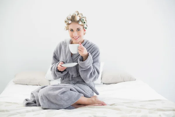 Cheerful relaxed blonde woman in hair curlers drinking coffee — Stock Photo, Image