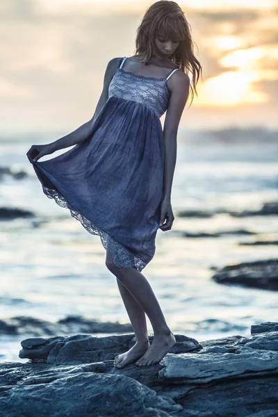 Beautiful young woman standing on rocks by the sea — Stock Photo, Image