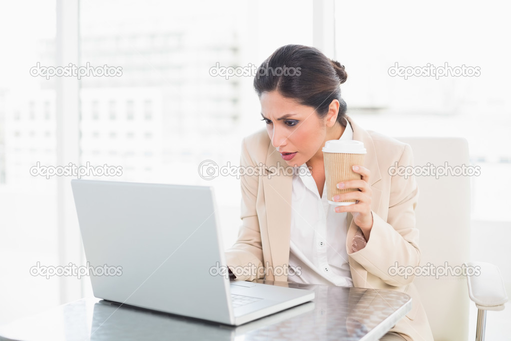 Concentrating businesswoman drinking coffee while working on laptop