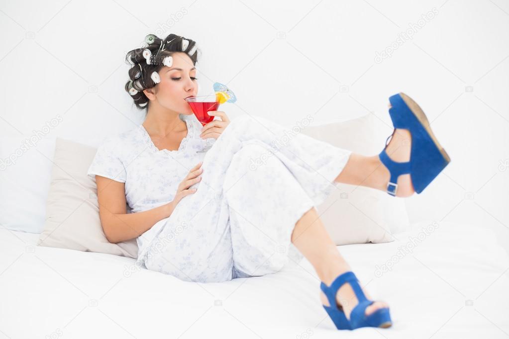 Brunette in hair rollers and wedge shoes drinking a cocktail