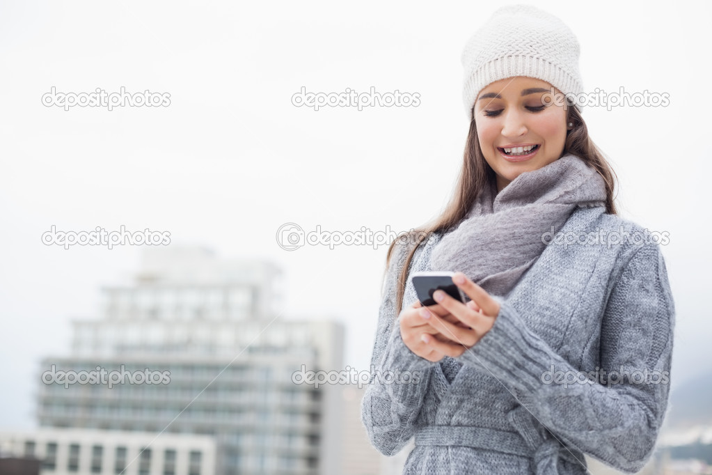 Smiling young woman with winter clothes on text messaging
