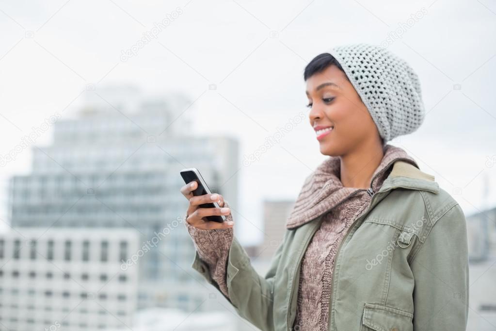 Amused young model in winter clothes looking at her mobile phone