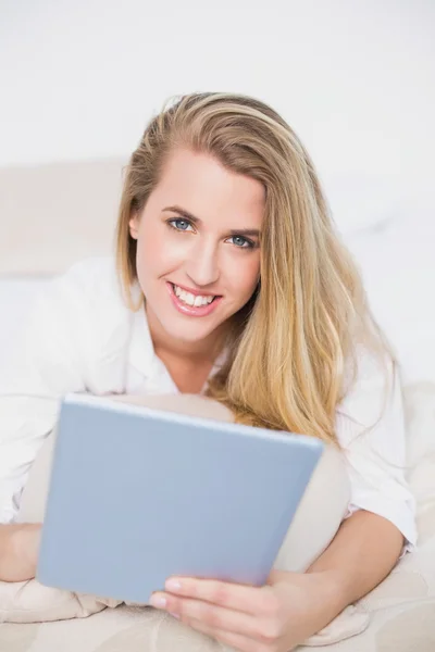 Modelo sonriente usando su tableta acostada en una cama acogedora —  Fotos de Stock