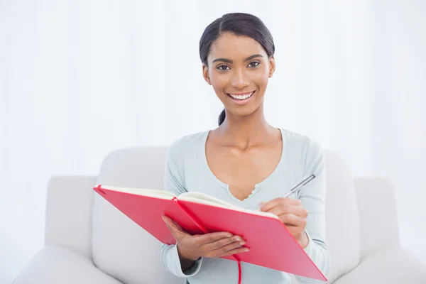 Fröhliche attraktive Frau sitzt auf gemütlichem Sofa und schreibt — Stockfoto