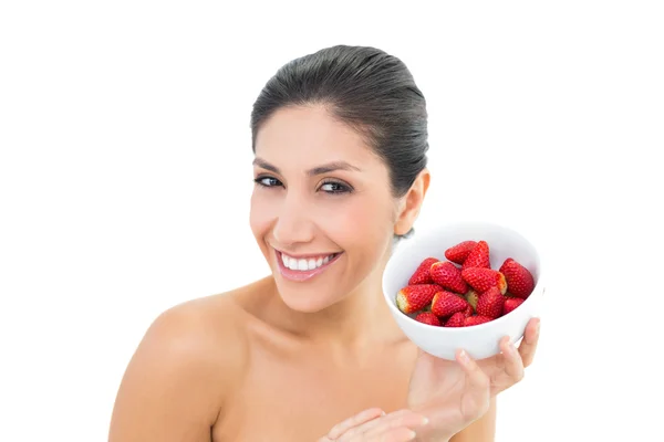 Pretty brunette holding a bowl of fresh strawberries and smiling at camera — Stock Photo, Image