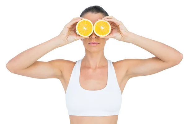 Fit woman holding slices of orange on her eyes — Stock Photo, Image