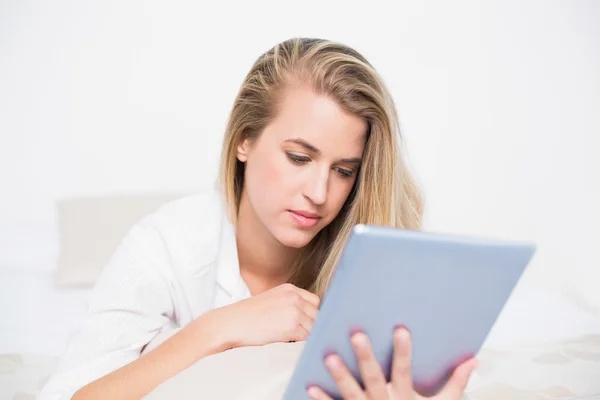 Focused pretty model using her tablet pc lying on cosy bed — Stock Photo, Image