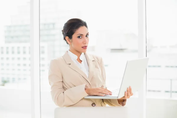 Frowning businesswoman standing behind her chair holding laptop — Stock Photo, Image